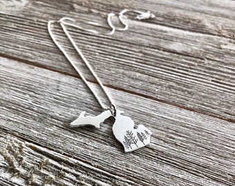 May include: A silver necklace with a pendant shaped like the state of Michigan. The pendant features a design of trees inside the state outline.