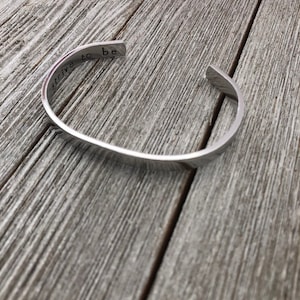 May include: A silver metal bracelet with the words "strive to be" engraved on it.