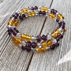 May include: A triple-strand bracelet made with clear, purple, and gold glass beads. The bracelet is wrapped around a silver wire.