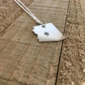 May include: A silver necklace with a pendant shaped like the state of Arizona. The pendant has a small cactus design engraved on it.