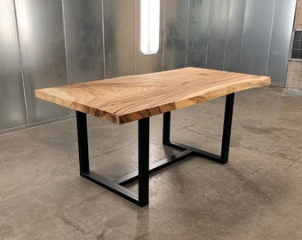 May include: A wooden dining table with a live edge top and black metal legs. The table is made of natural wood with a light brown finish. The legs are made of sturdy metal and have a black powder coat finish.