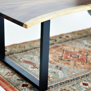 May include: A wooden table top with a live edge and a black metal base. The table is sitting on a patterned rug.