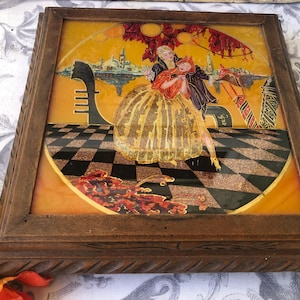 Może przedstawiać: Ramka z obrazem o złotym tle przedstawiającym scenę z dwojgiem tańczących osób. Obraz umieszczony jest na szachownicy i przedstawia panoramę miasta w tle.