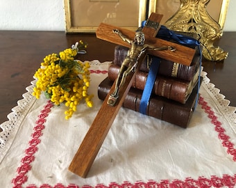 Op de afbeelding: Een houten kruisbeeld met een gouden Jezusfiguur, rustend op een stapel van drie in leer gebonden boeken. Een boeket gele mimosa's ligt op een wit kantkleed.