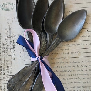 Pode incluir: Um conjunto de seis colheres de prata antigas amarradas com uma fita rosa e azul. As colheres têm tigelas em forma de coração e alças ornamentadas.