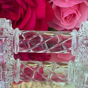 May include: Clear glass cabinet knobs with a decorative floral design on the ends and a twisted, ridged center. The knobs are set against a backdrop of vibrant pink and red roses, creating a striking contrast.