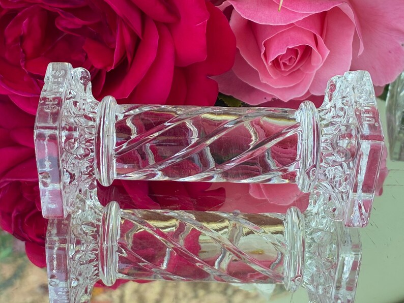May include: Clear glass cabinet knobs with a decorative floral design on the ends and a twisted, ridged center. The knobs are set against a backdrop of vibrant pink and red roses, creating a striking contrast.