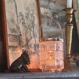 May include: A clear glass bucket with a textured, geometric hobnail pattern and a silver-toned metal handle. The cylindrical container features a repeating grid of raised squares and circular motifs, reflecting light from within.