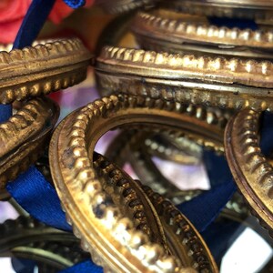May include: Close-up of several antique gold-colored picture frame ornaments with ornate, textured edges. Each frame has a blue ribbon attached. The frames are clustered together, creating a layered effect. The overall theme is vintage decor.