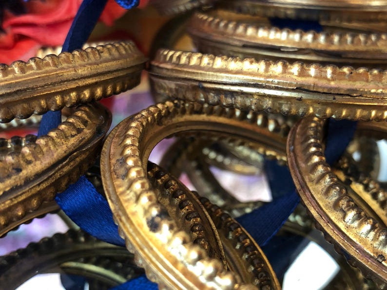 May include: Close-up of several antique gold-colored picture frame ornaments with ornate, textured edges. Each frame has a blue ribbon attached. The frames are clustered together, creating a layered effect. The overall theme is vintage decor.