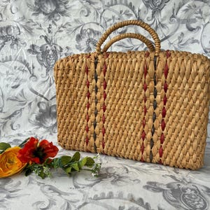 May include: A woven straw handbag with red and blue stripes. The bag has two handles and is made of natural materials.
