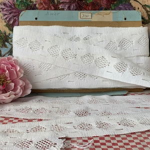 May include: White cotton lace trim with a delicate pattern of small circles and a scalloped edge. The lace is approximately 1 inch wide and is shown on a checkered fabric background.
