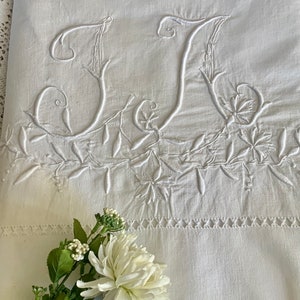 May include: White linen pillowcase with a delicate embroidered design featuring the letters "JJ" in a script font. The embroidery is surrounded by a floral pattern.