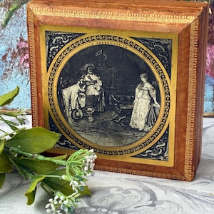 Op de afbeelding: Een rechthoekige, antieke houten doos met een ingelijste illustratie. De ronde illustratie toont een historische scène met figuren in historische kleding. De doos heeft een gouden rand en de tekst "LA PRESENTATION".
