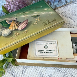 May include: Vintage Suchard chocolate box with a seashell design. The box is open, revealing old papers and a label from Laboratoires Dejardin-Basset. The box lid features the word "Coquillages" and the words "MOULAGES EN CHOCOLAT AU LAIT".