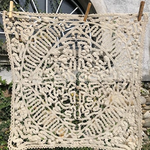 Può includere: Un delicato tovagliolo in pizzo all'uncinetto color crema con un intricato motivo circolare. Il pizzo è appeso a uno stendino.