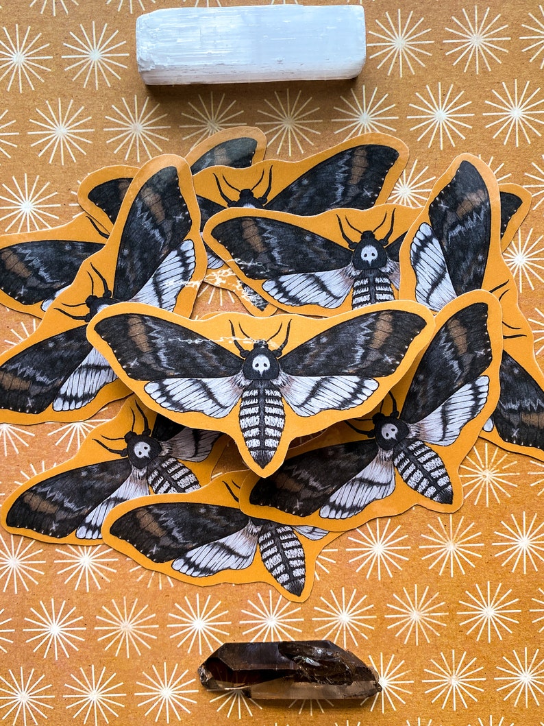May include: A collection of black and white moth stickers with a skull design on a yellow background with white starburst patterns.