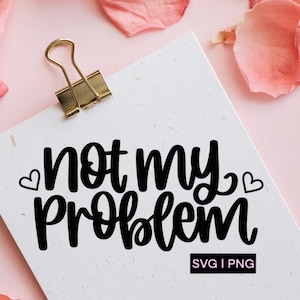 Pode incluir: Um cartão branco com o texto "not my problem" escrito em fonte cursiva preta. Dois pequenos corações estão de cada lado do texto. O cartão está preso a um fundo rosa com pétalas de rosa rosa.
