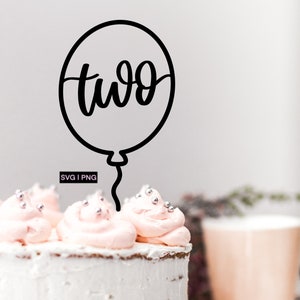 May include: A white frosted cake decorated with pink frosting, silver sprinkles, and red and pink heart-shaped sprinkles. A black balloon cake topper with the word "two" is placed on top. The cake sits on a silver cake board.