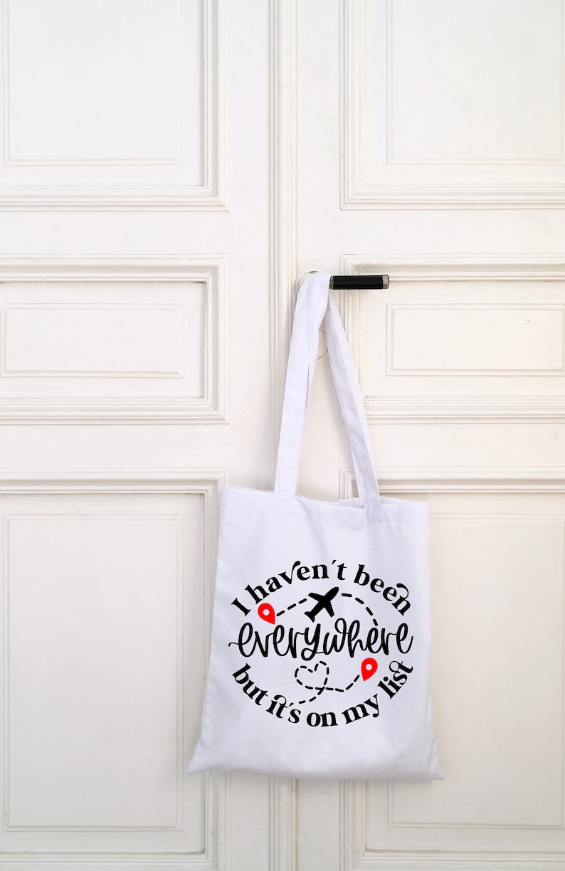 May include: White canvas tote bag with black text that reads "I haven't been everywhere but it's on my list". The text is in a circle with a plane and red location pins.