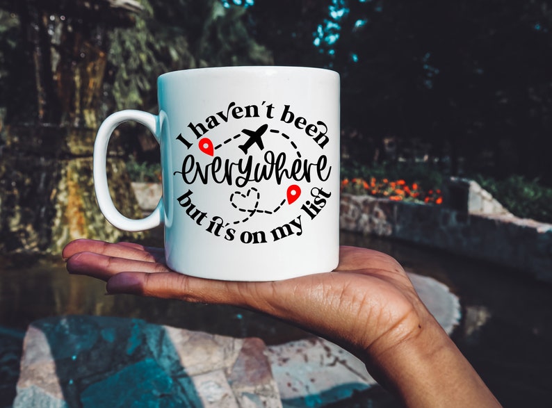 May include: White ceramic mug with a black graphic that reads "I haven't been everywhere but it's on my list". The graphic includes a plane, a heart, and two red location pins.