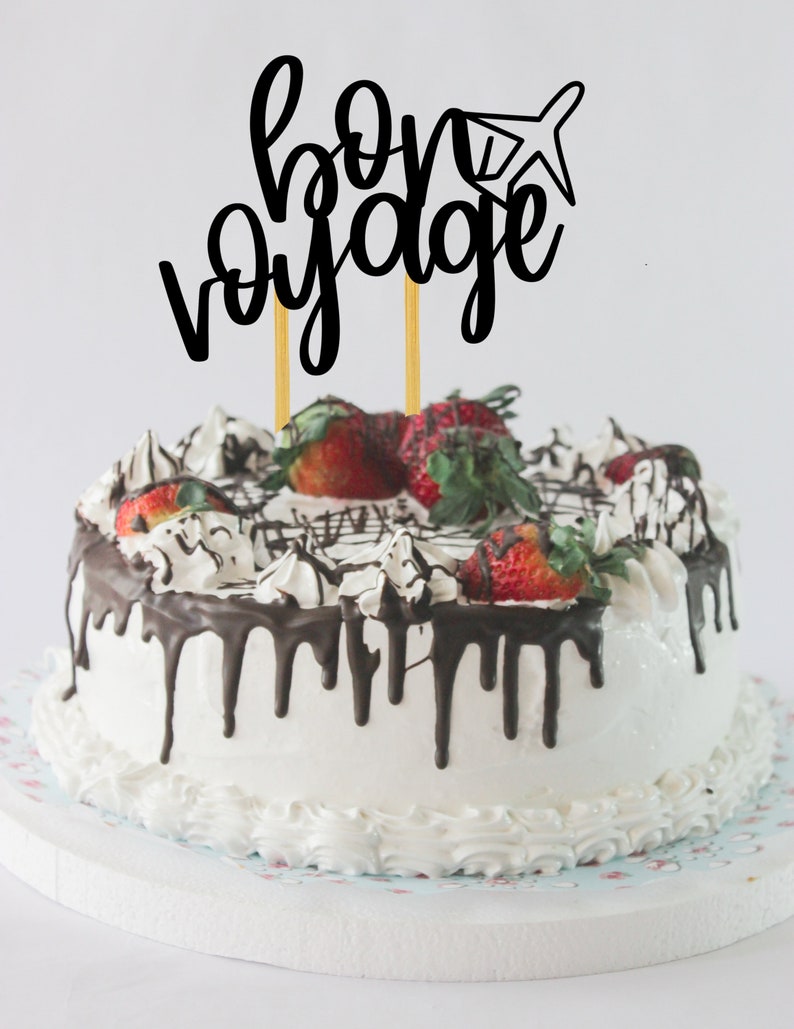 May include: A white cake with chocolate frosting and strawberries, topped with a black cake topper that says "bon voyage" with a small airplane graphic.