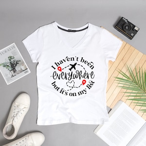 May include: White v-neck t-shirt with a black graphic that says "I haven't been everywhere but it's on my list" with a plane and red pins.