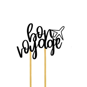 May include: Black and white cake topper with the text "bon voyage" and a small airplane graphic. The topper is on two gold sticks.