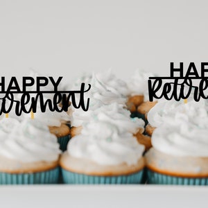 May include: A tray of cupcakes with white icing and blue cases. Two of the cupcakes have black toppers that say "Happy Retirement".