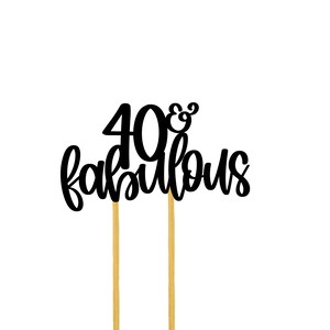 May include: Black cake topper with the text "40 & fabulous" on two gold sticks.
