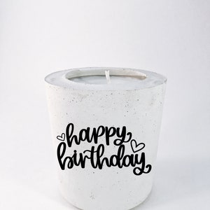 May include: White concrete candle holder with a black inscription that reads "happy birthday" with two small hearts.