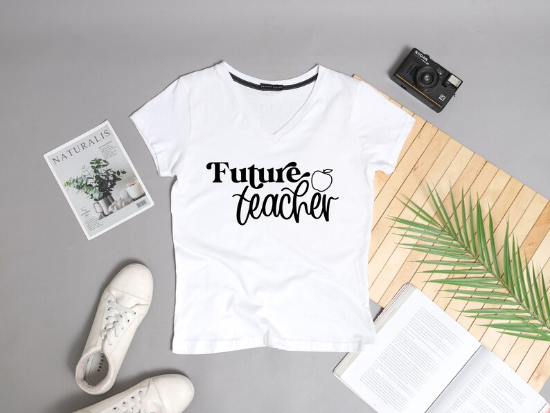 May include: White v-neck t-shirt with the text "Future Teacher" and a red apple graphic.