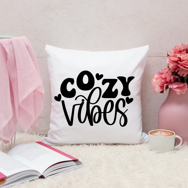 Puede incluir: Almohada blanca con texto negro que dice "cozy vibes" y peque&ntilde;os corazones.