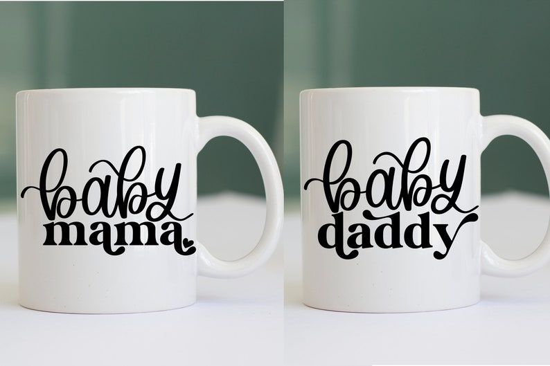 May include: Two white ceramic mugs with black lettering. The mug on the left says "baby mama" and the mug on the right says "baby daddy".