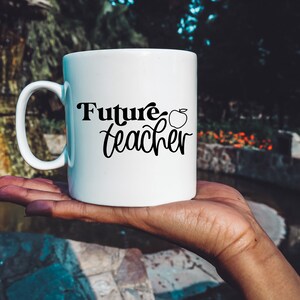 May include: White ceramic mug with a black inscription that reads "Future teacher" with a small apple graphic next to the text.