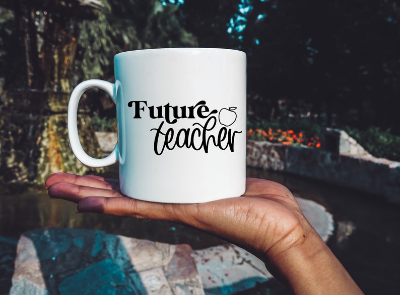 May include: White ceramic mug with a black inscription that reads "Future teacher" with a small apple graphic next to the text.