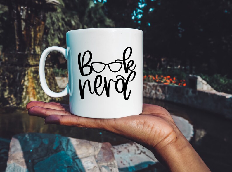 May include: White ceramic mug with a black design that says "Book Nerd" with a pair of glasses above the word "Nerd".