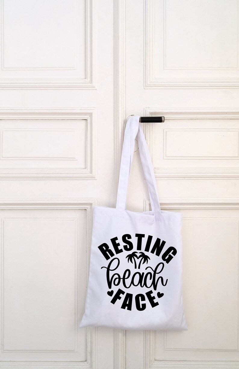 Może przedstawiać: Biała torba typu tote z czarnym tekstem, kt&oacute;ry brzmi "Resting Beach Face" z grafiką palmy.