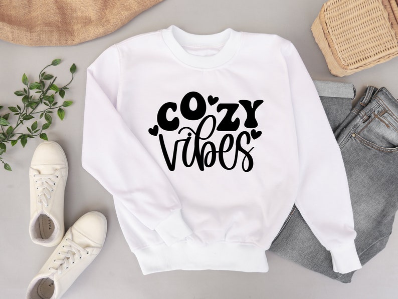 Puede incluir: Sudadera blanca con texto negro que dice "cozy vibes" con corazones alrededor de las letras.