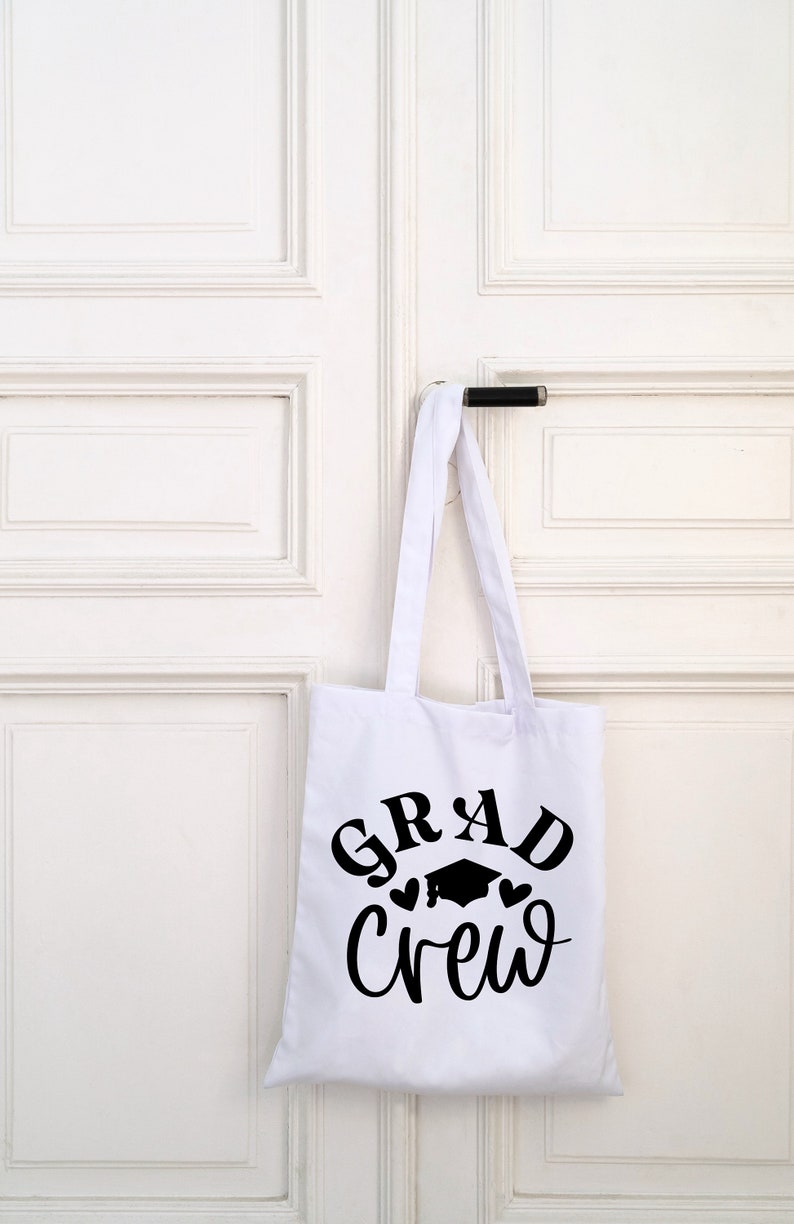 May include: White tote bag with black text that reads "GRAD Crew" with a graduation cap and two hearts.