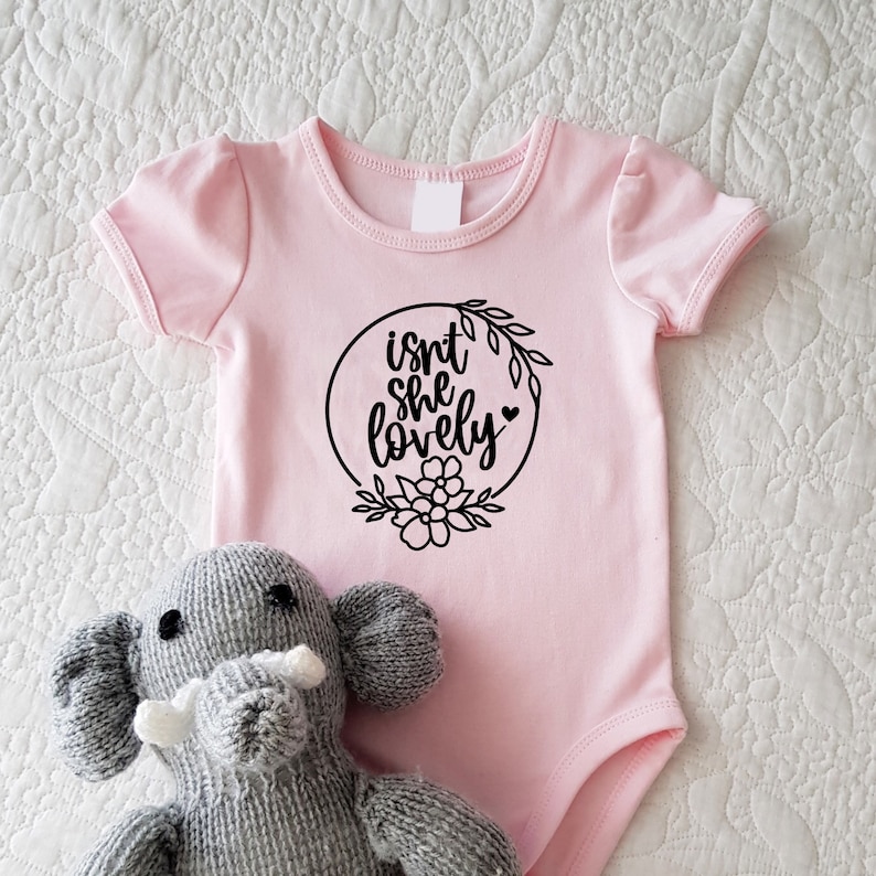 May include: Pink baby onesie with black text that reads "isn't she lovely" inside a circle with floral accents.