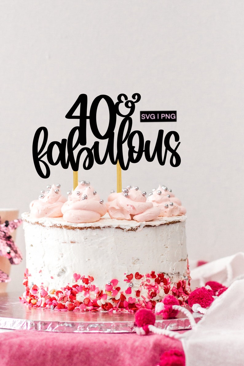 May include: A white cake with pink frosting and sprinkles, topped with a black cake topper that says "40 & fabulous" with a gold accent. The cake topper is on two gold sticks.