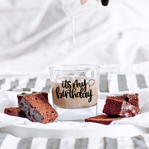 K&ouml;nnte beinhalten: Ein Glas Schokoladenmilch mit dem Text "it's my birthday" an der Seite. Auf einer wei&szlig;-grauen gestreiften Oberfl&auml;che liegen mehrere St&uuml;cke Schokoladenkuchen.