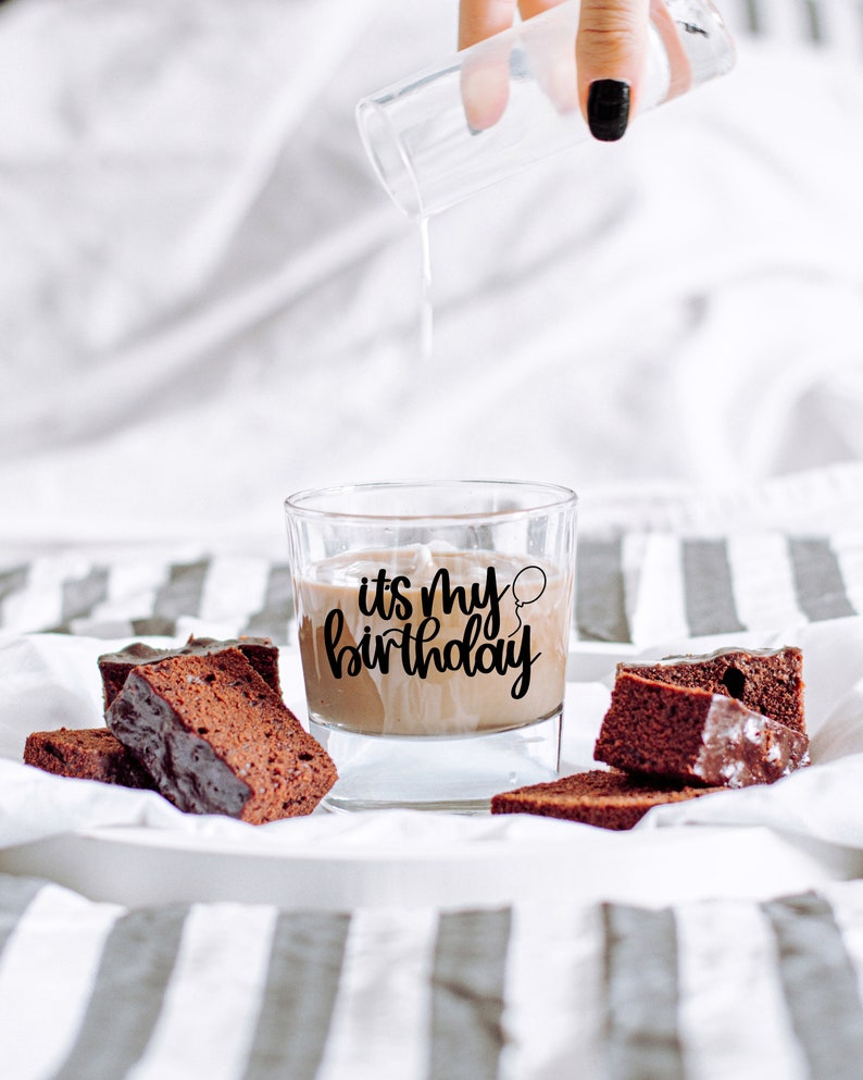 K&ouml;nnte beinhalten: Ein Glas Schokoladenmilch mit dem Text "it's my birthday" an der Seite. Auf einer wei&szlig;-grauen gestreiften Oberfl&auml;che liegen mehrere St&uuml;cke Schokoladenkuchen.
