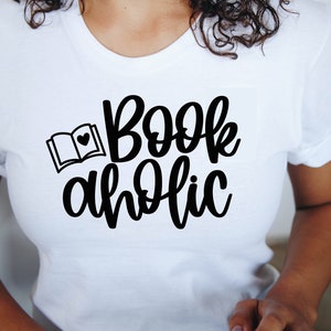 May include: White t-shirt with black text that reads "Bookaholic" and a small black illustration of an open book with a heart on the page.