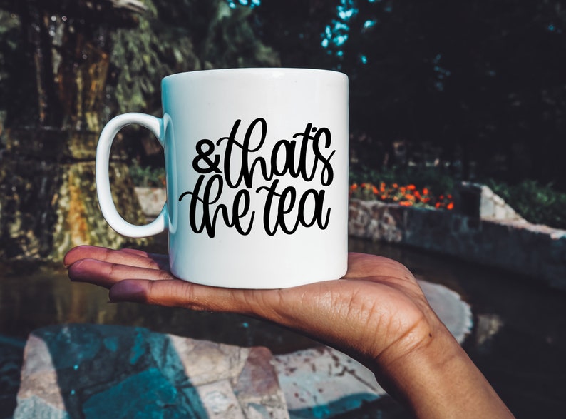 May include: White ceramic mug with a black cursive inscription that reads "& that's the tea".