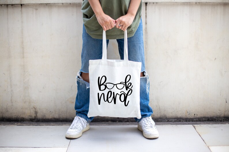 May include: A white tote bag with the text "book nerd" and a pair of glasses printed on it.