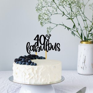 May include: White cake with white frosting decorated with blueberries and blackberries. The cake has a black topper that says "40 & fabulous".