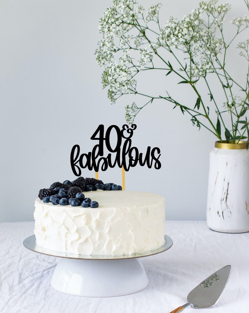 May include: White cake with white frosting decorated with blueberries and blackberries. The cake has a black topper that says "40 & fabulous".