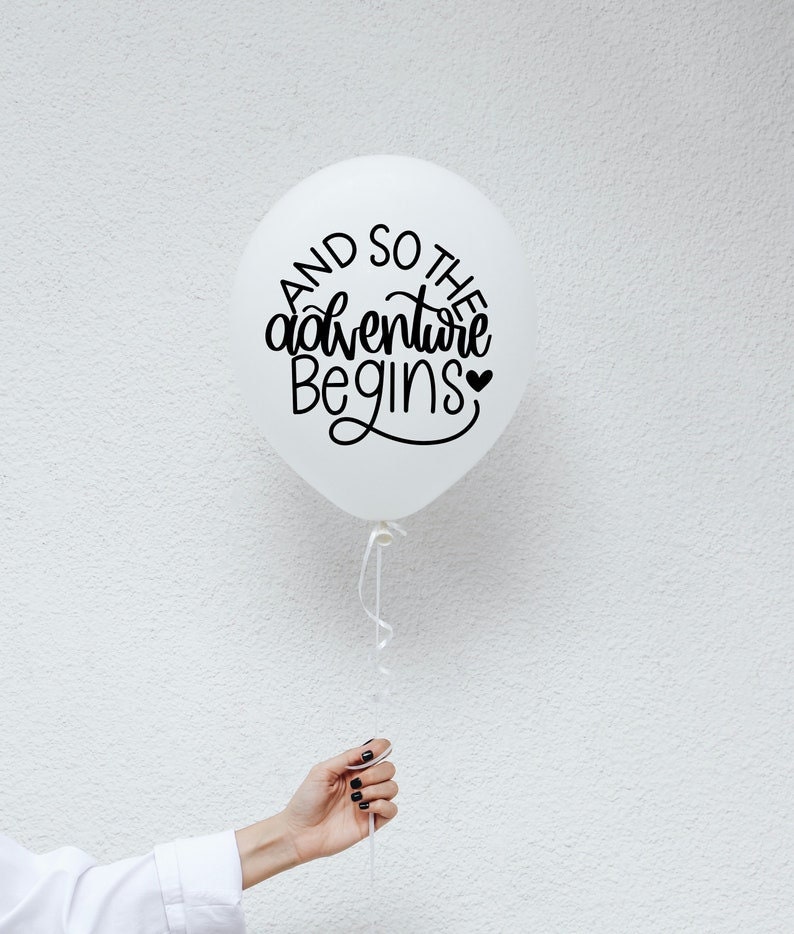 May include: White balloon with black lettering that reads "And so the adventure begins" with a small heart symbol.